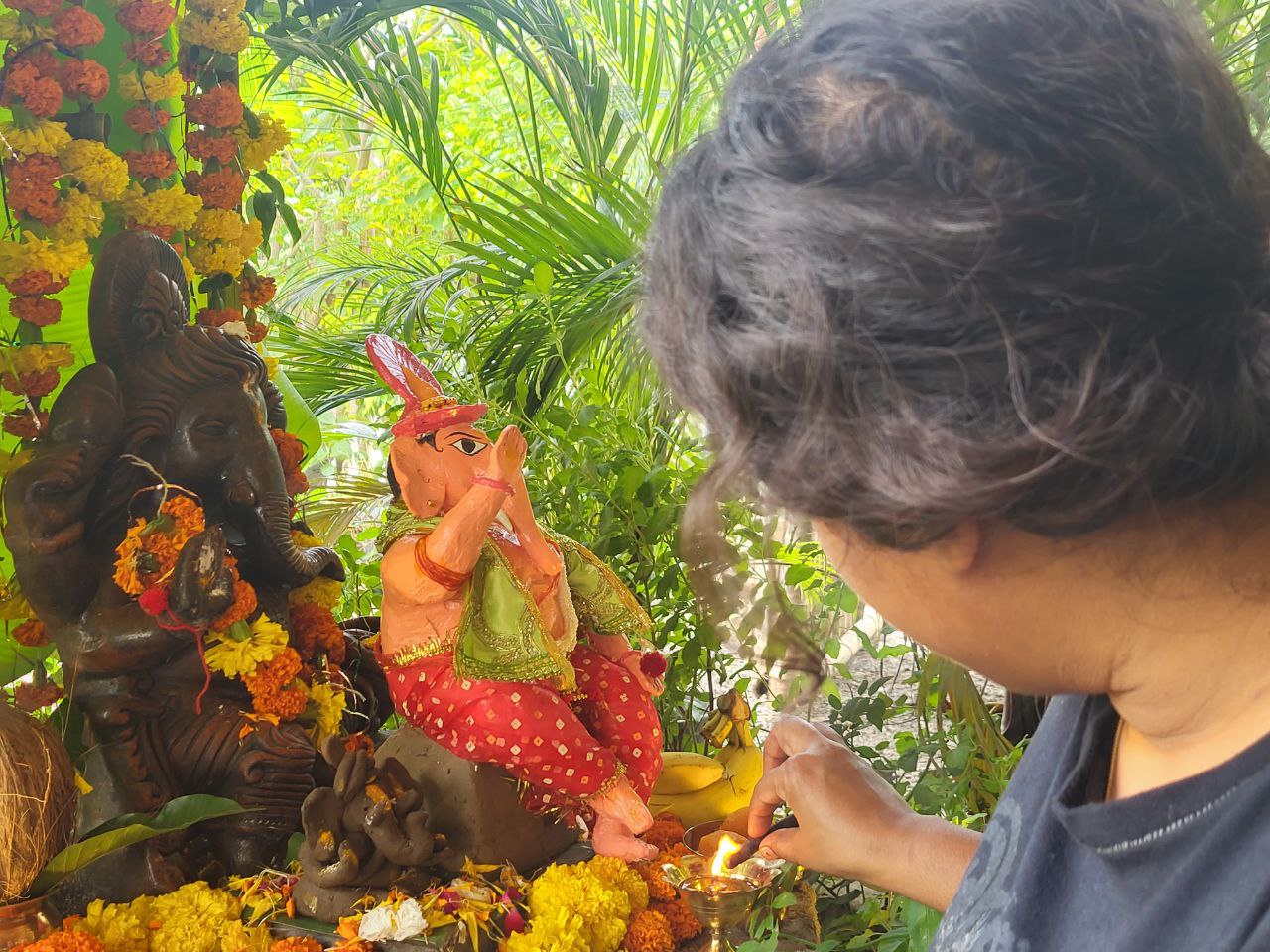 A person lighting a diya in front of a Ganesha idol